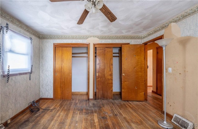 unfurnished bedroom with wallpapered walls, baseboards, dark wood-style flooring, ornate columns, and multiple closets