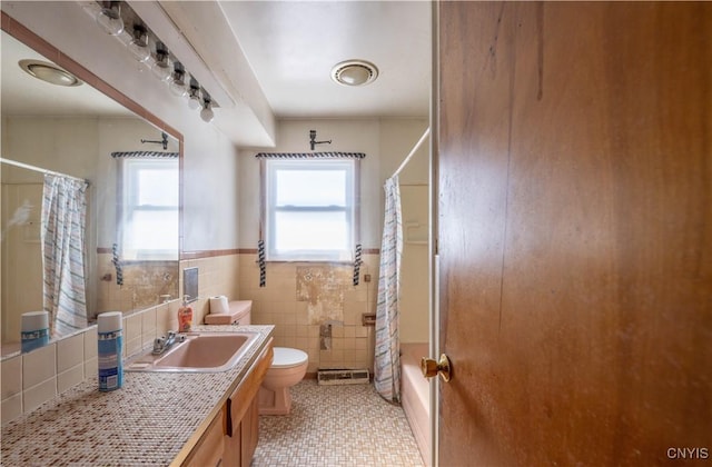 full bathroom featuring a wainscoted wall, shower / tub combo with curtain, tile walls, toilet, and vanity