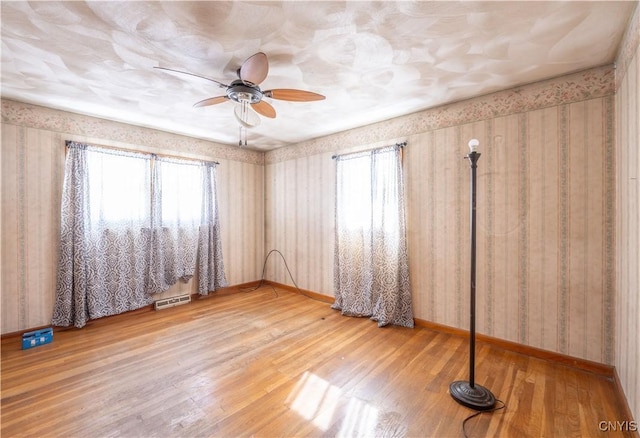 unfurnished bedroom featuring baseboards, wood finished floors, visible vents, and wallpapered walls