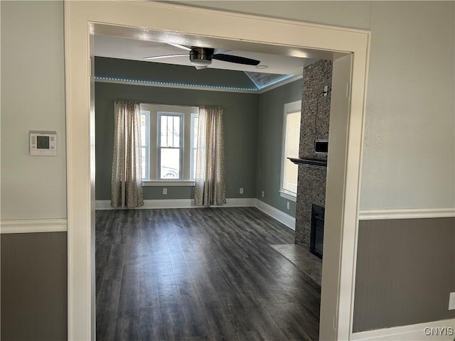 unfurnished living room featuring ceiling fan, a fireplace, dark wood-style floors, and baseboards