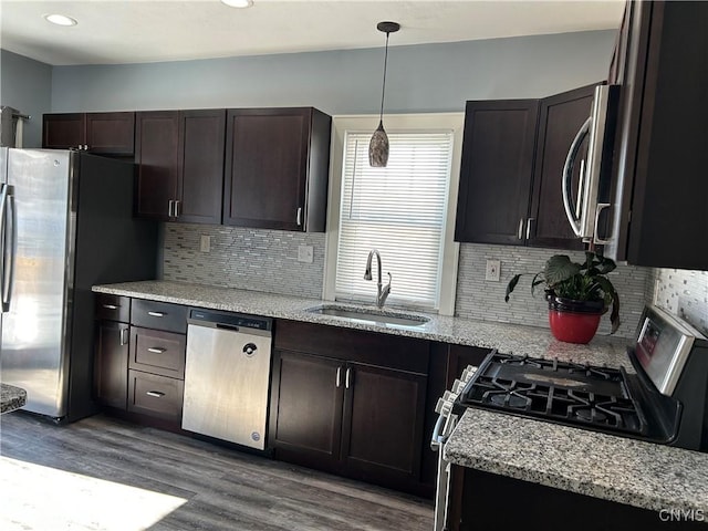 kitchen featuring dark brown cabinetry, appliances with stainless steel finishes, light stone counters, hanging light fixtures, and a sink