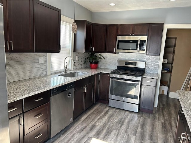 kitchen featuring light stone counters, dark wood-style flooring, pendant lighting, stainless steel appliances, and a sink