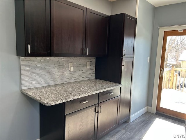 kitchen featuring baseboards, light wood-style flooring, light stone countertops, dark brown cabinets, and backsplash