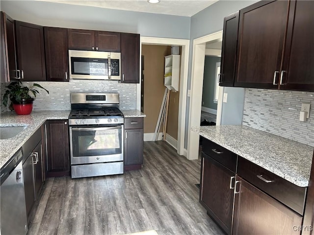 kitchen with stainless steel appliances, dark brown cabinets, dark wood-style flooring, and light stone counters