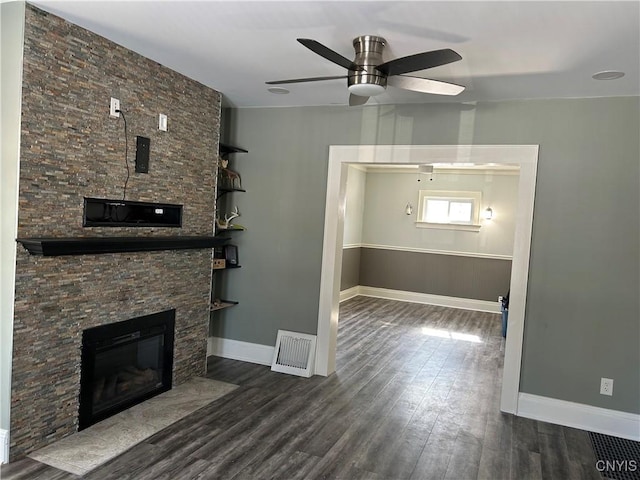 unfurnished living room with dark wood-style flooring, visible vents, a ceiling fan, a stone fireplace, and baseboards