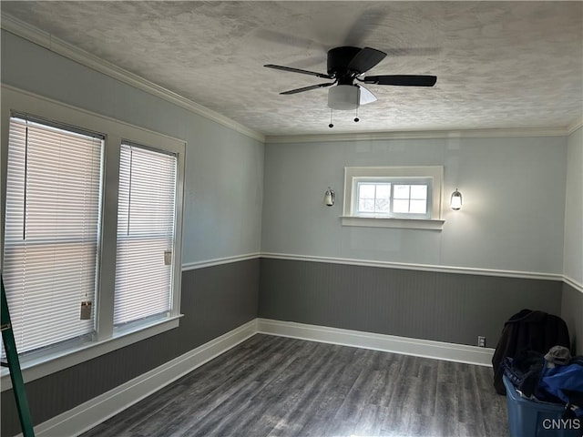 empty room featuring a wainscoted wall, crown molding, dark wood-type flooring, a textured ceiling, and baseboards