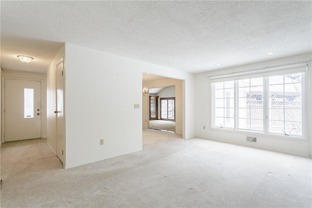 spare room featuring light carpet, a textured ceiling, visible vents, and baseboards