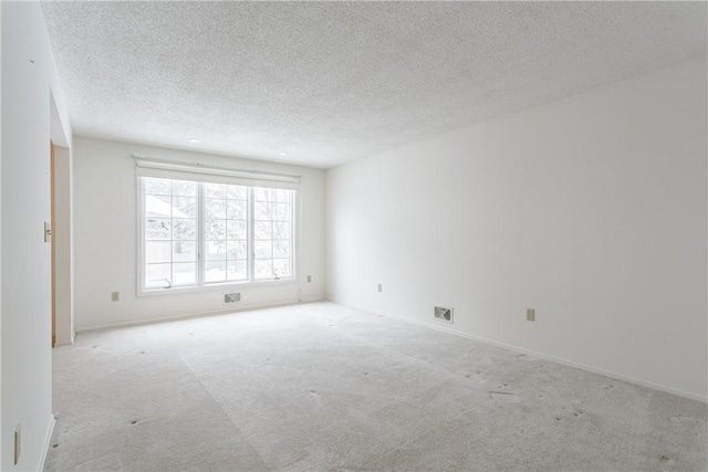 empty room with baseboards, visible vents, light carpet, and a textured ceiling