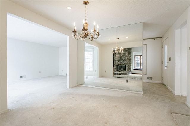 unfurnished living room featuring light carpet, recessed lighting, a fireplace, and a notable chandelier