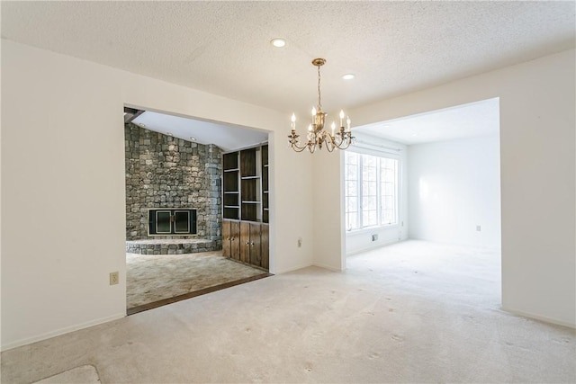 unfurnished dining area with a textured ceiling, a stone fireplace, carpet flooring, and a chandelier