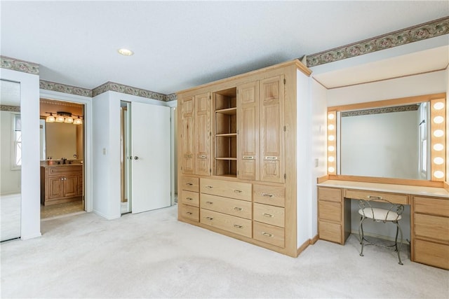 bedroom featuring ensuite bathroom, light colored carpet, a sink, baseboards, and built in study area