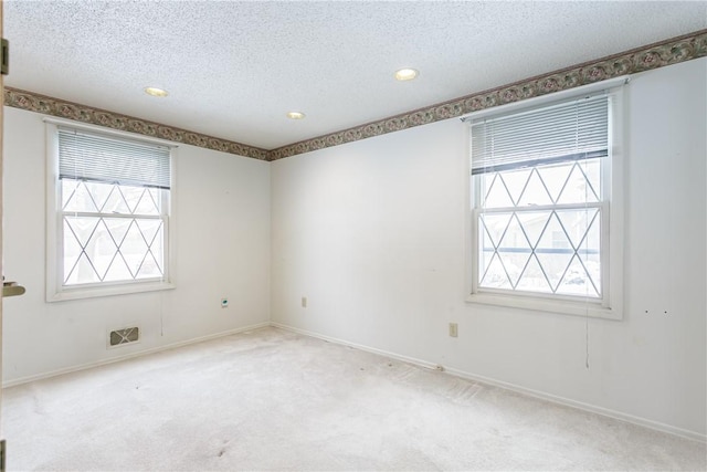 empty room featuring a textured ceiling, baseboards, visible vents, and light colored carpet