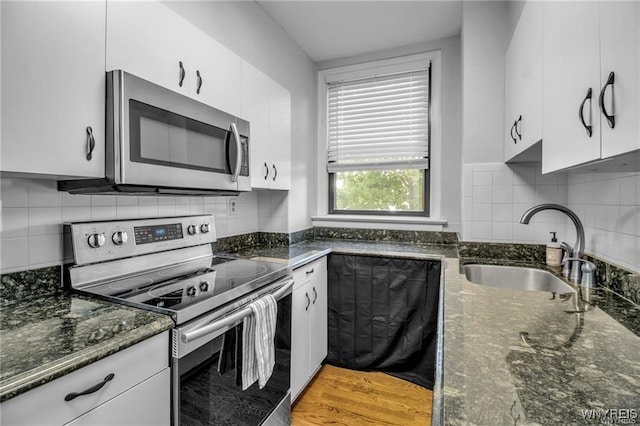 kitchen featuring stainless steel appliances, tasteful backsplash, white cabinets, a sink, and dark stone countertops