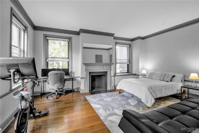 bedroom with a fireplace with flush hearth, crown molding, baseboards, and wood finished floors