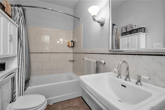 full bathroom featuring tile walls, shower / bath combination with curtain, toilet, wainscoting, and a sink