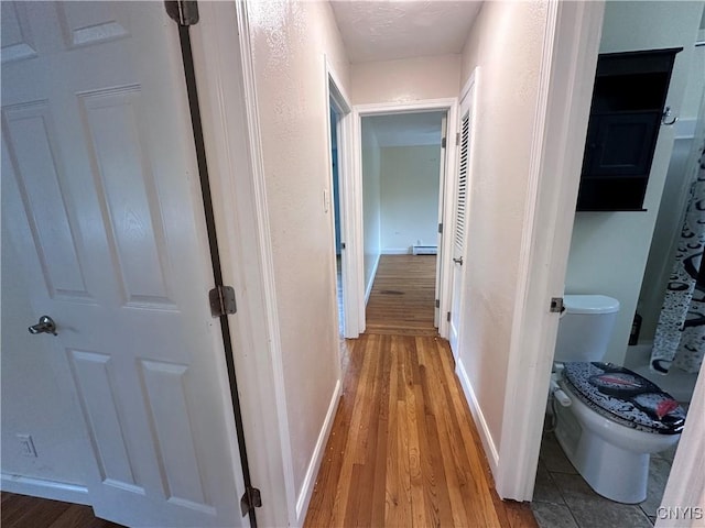 hallway with a baseboard heating unit, light wood-type flooring, and baseboards