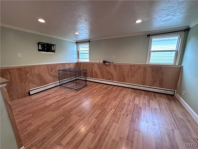 empty room with wainscoting, ornamental molding, wood finished floors, a baseboard heating unit, and recessed lighting