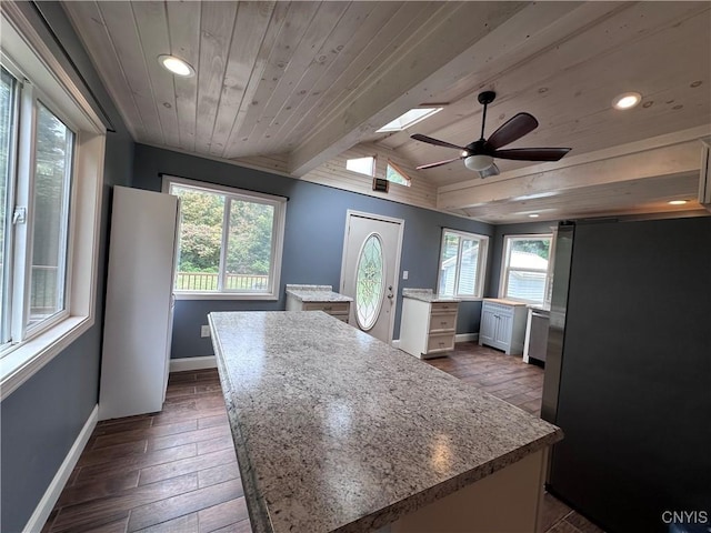 kitchen with freestanding refrigerator, a center island, a healthy amount of sunlight, and baseboards