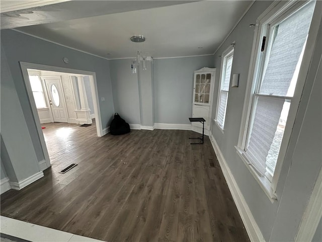 unfurnished living room featuring crown molding, dark wood-type flooring, visible vents, and baseboards