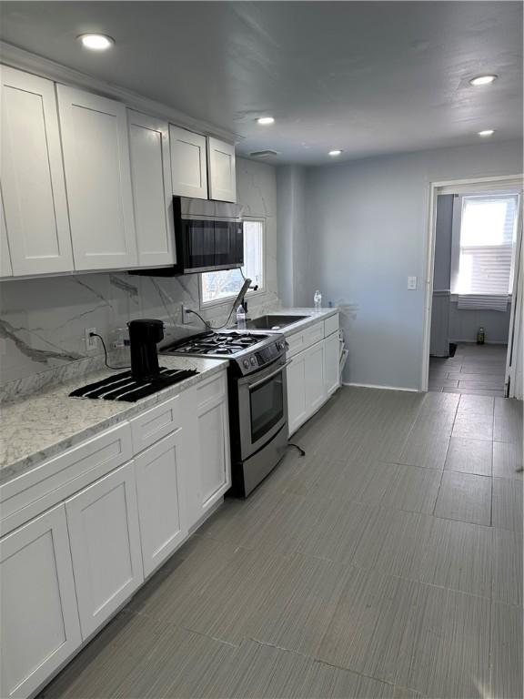 kitchen featuring light stone counters, a sink, white cabinets, appliances with stainless steel finishes, and tasteful backsplash