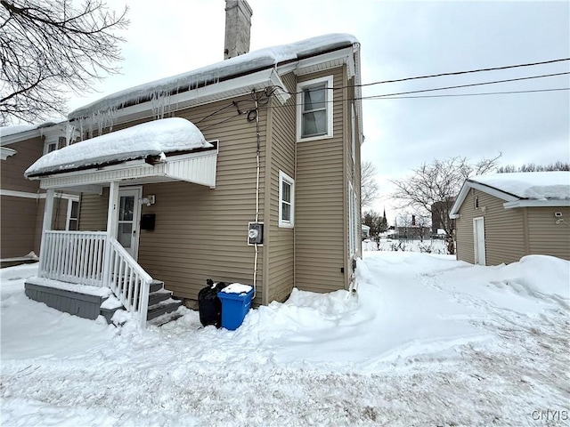 snow covered back of property with a garage and a chimney