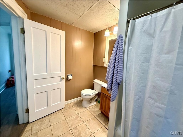 bathroom featuring a drop ceiling, tile patterned flooring, toilet, wood walls, and vanity