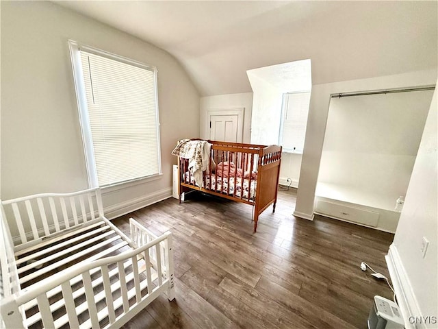 bedroom featuring lofted ceiling, dark wood-style floors, baseboards, and a crib