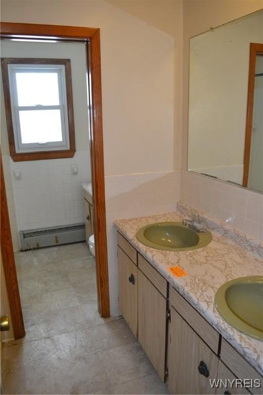 full bath featuring double vanity, baseboard heating, a sink, and toilet