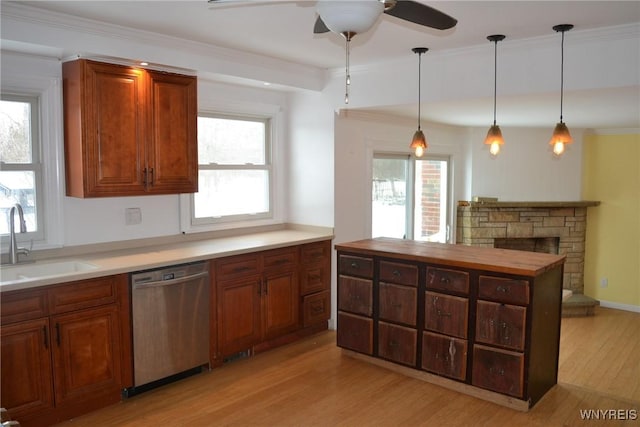 kitchen featuring a sink, stainless steel dishwasher, light wood-type flooring, a wealth of natural light, and decorative light fixtures