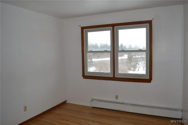 spare room with a baseboard heating unit, wood finished floors, and baseboards