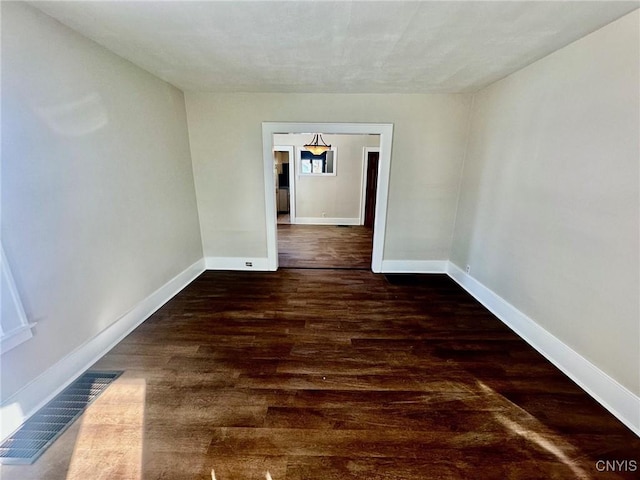 unfurnished room featuring baseboards, visible vents, and dark wood-style flooring