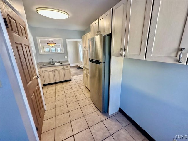 kitchen with baseboards, freestanding refrigerator, light countertops, a sink, and light tile patterned flooring