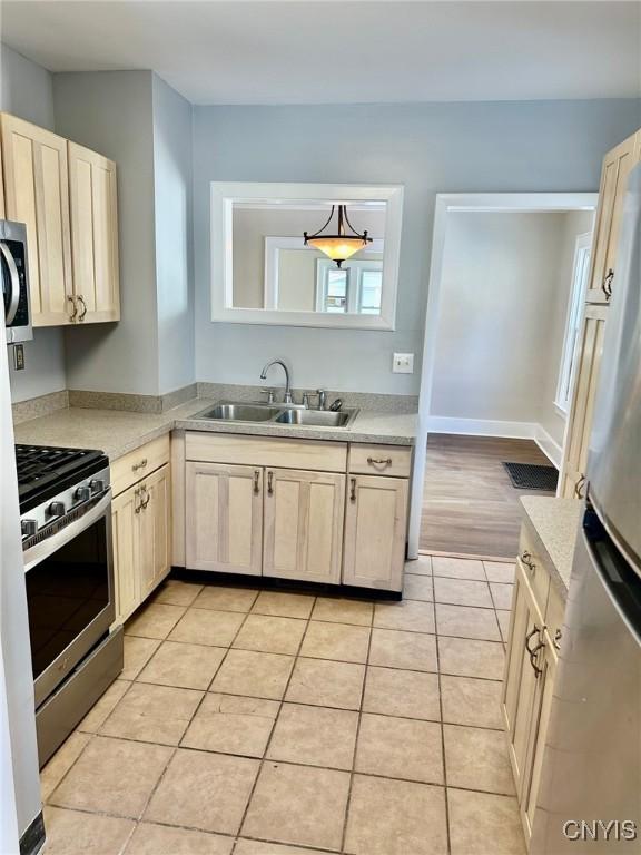 kitchen featuring baseboards, stainless steel appliances, light countertops, a sink, and light tile patterned flooring