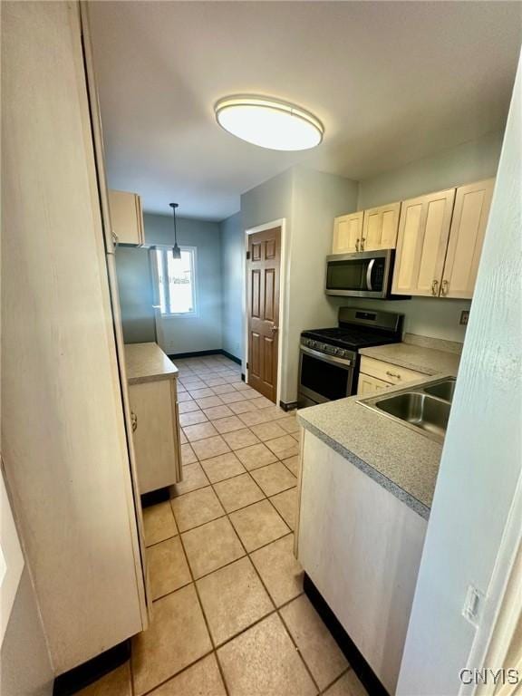 kitchen with light tile patterned flooring, a sink, light countertops, appliances with stainless steel finishes, and decorative light fixtures