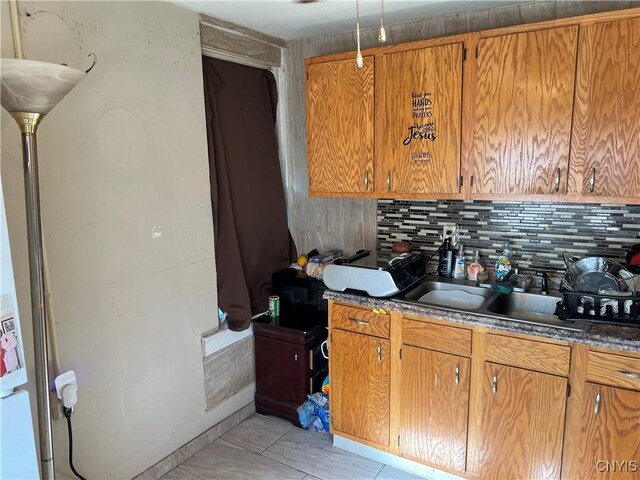 kitchen featuring tasteful backsplash, brown cabinetry, dark countertops, and a sink