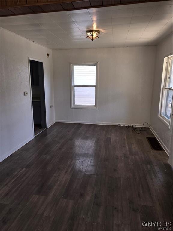 empty room with dark wood-style floors, visible vents, a wealth of natural light, and baseboards