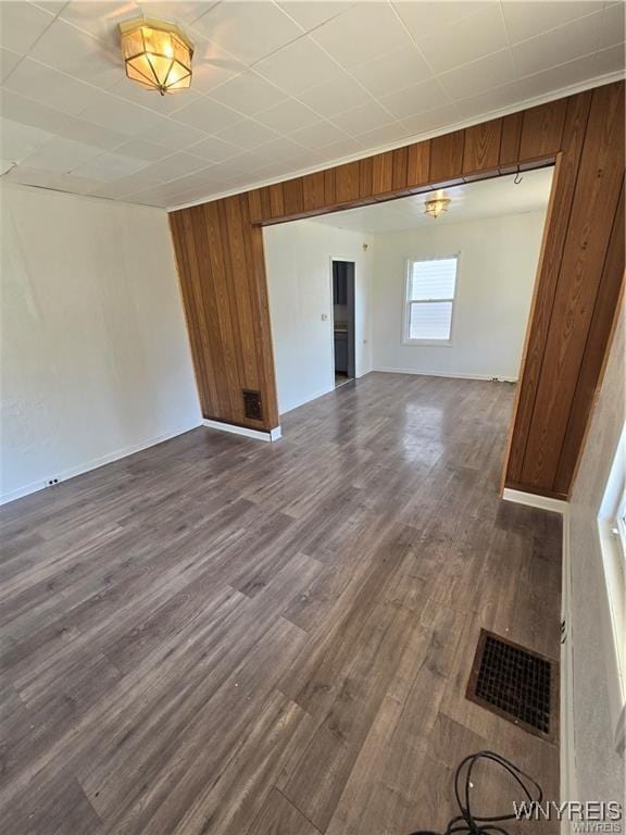 unfurnished room with visible vents, dark wood finished floors, and wood walls