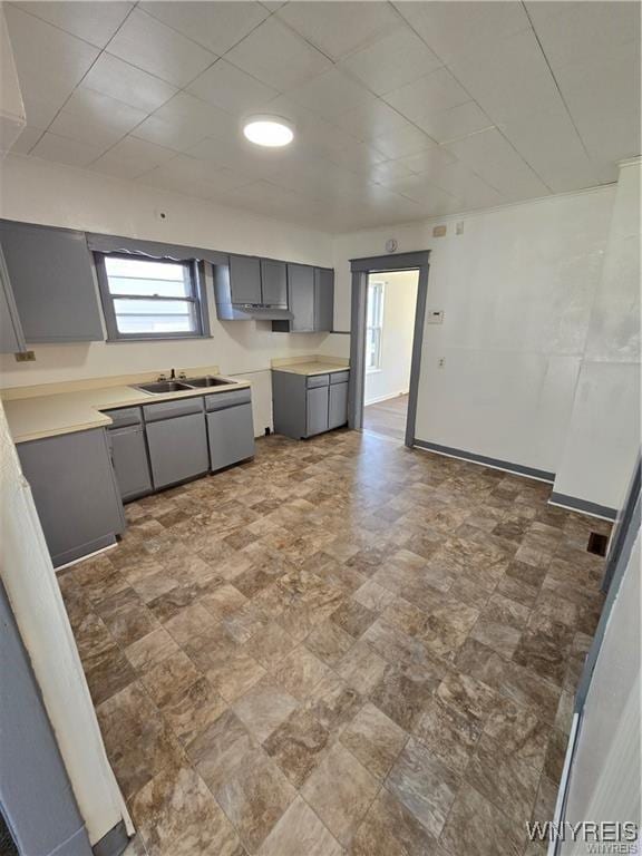 kitchen with gray cabinets, light countertops, a sink, and baseboards