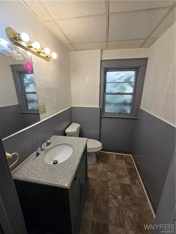 bathroom featuring toilet, stone finish floor, a drop ceiling, and vanity