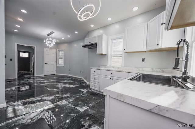 kitchen with under cabinet range hood, white cabinetry, light countertops, and a sink