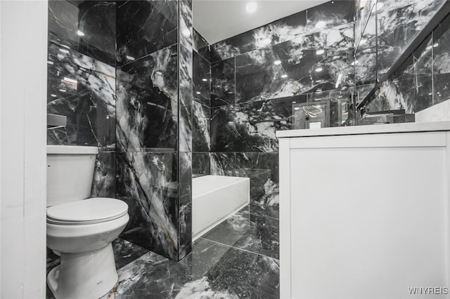 bathroom with toilet, a bathing tub, marble finish floor, vanity, and tile walls