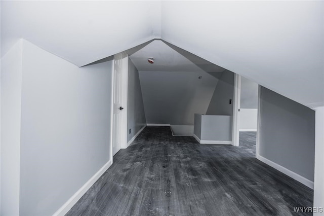 additional living space featuring baseboards, vaulted ceiling, and dark wood-type flooring