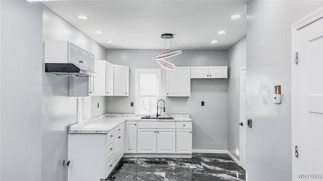 kitchen featuring marble finish floor, decorative light fixtures, light countertops, white cabinetry, and a sink