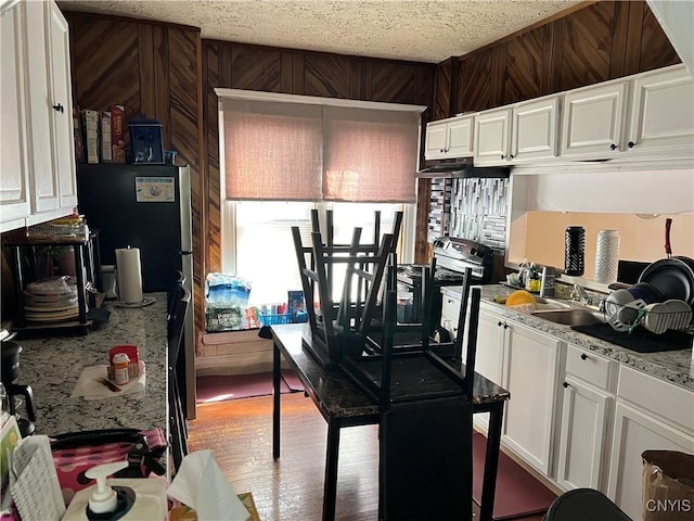 kitchen with white cabinets, a sink, wooden walls, and a textured ceiling