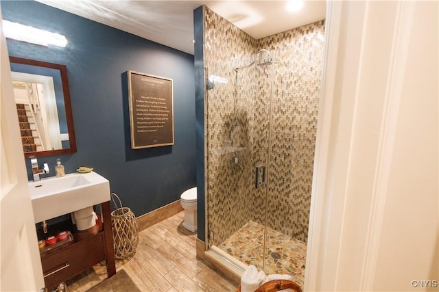 bathroom featuring toilet, a stall shower, a sink, wood finished floors, and baseboards