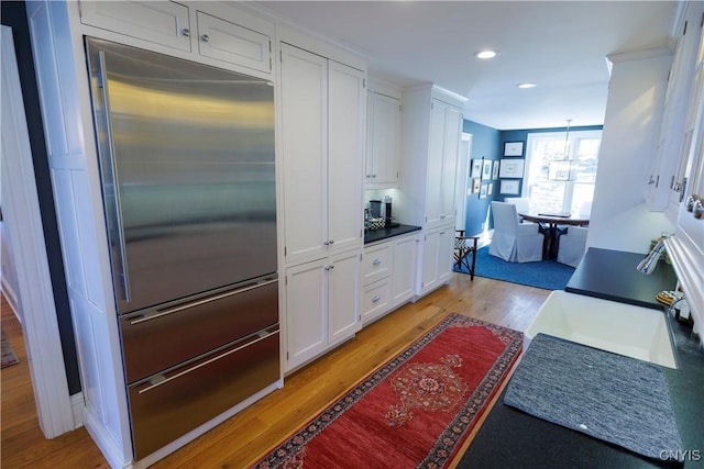 kitchen with light wood-style flooring, recessed lighting, white cabinets, stainless steel built in refrigerator, and dark countertops