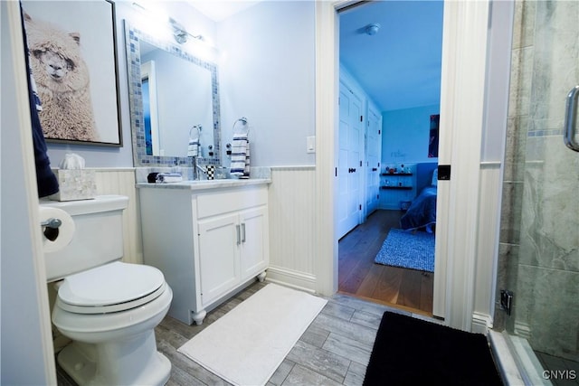 ensuite bathroom with wood finish floors, a wainscoted wall, vanity, and ensuite bath