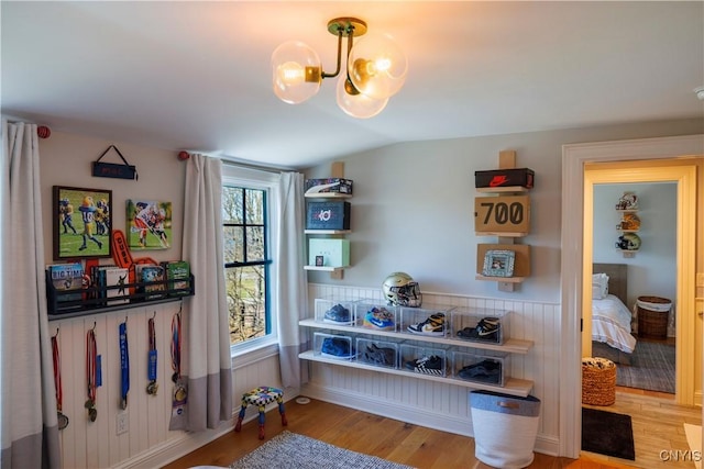 interior space with lofted ceiling, an inviting chandelier, wood finished floors, and a wainscoted wall