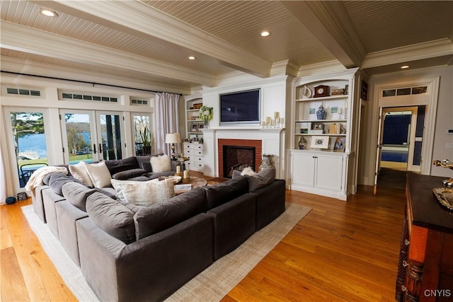 living area featuring light wood finished floors, ornamental molding, beamed ceiling, french doors, and a brick fireplace