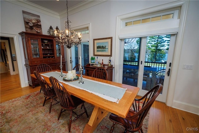 dining area with baseboards, light wood finished floors, an inviting chandelier, and crown molding